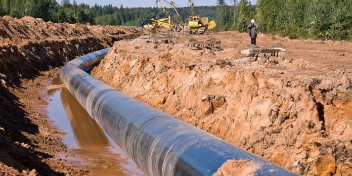 Conduite de pipeline en cours d’installation dans une tranchée, avec engins de chantier et ouvriers au loin